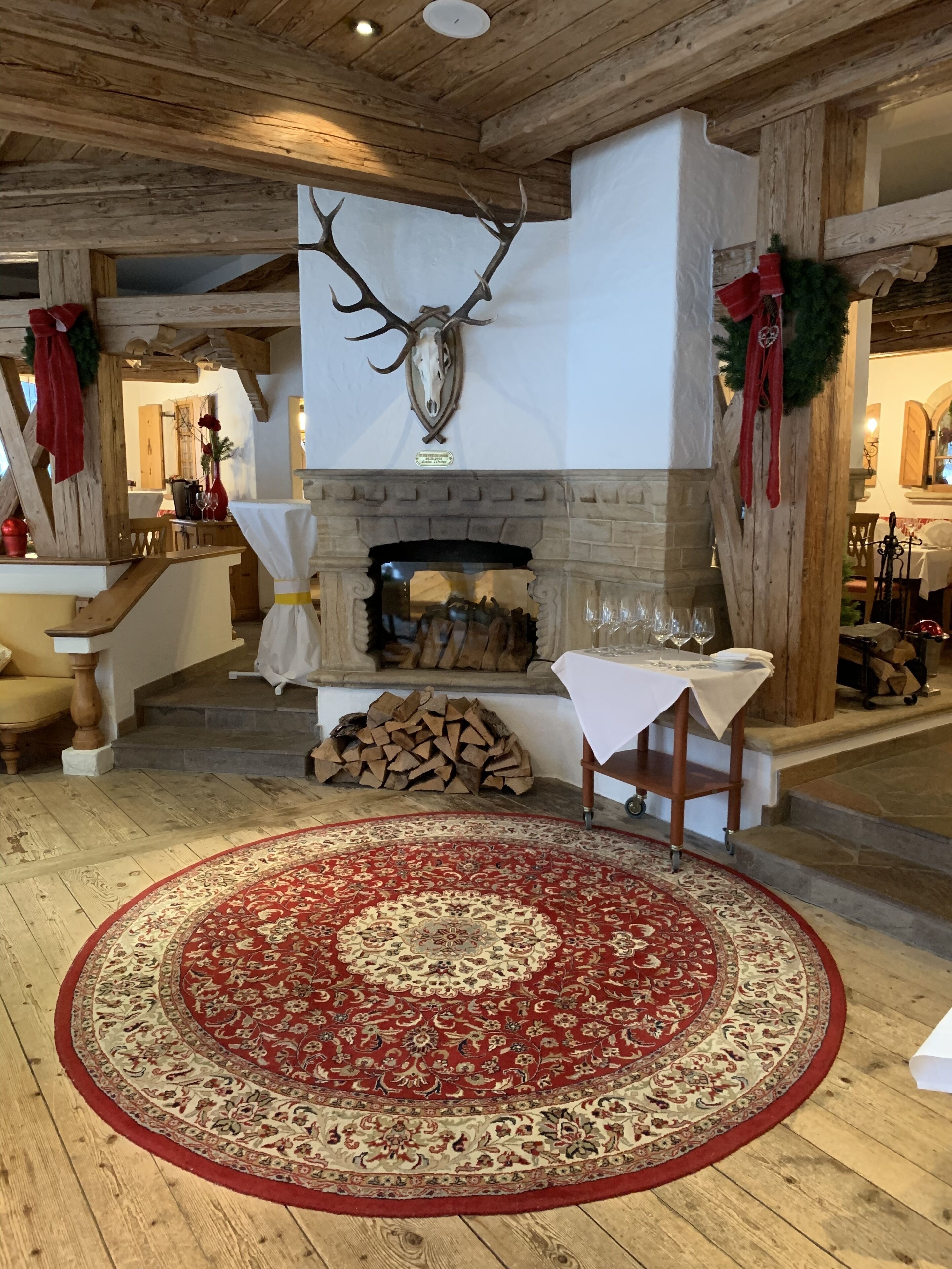 A rustic interior with a stone fireplace, a mounted deer head, and a red patterned rug.