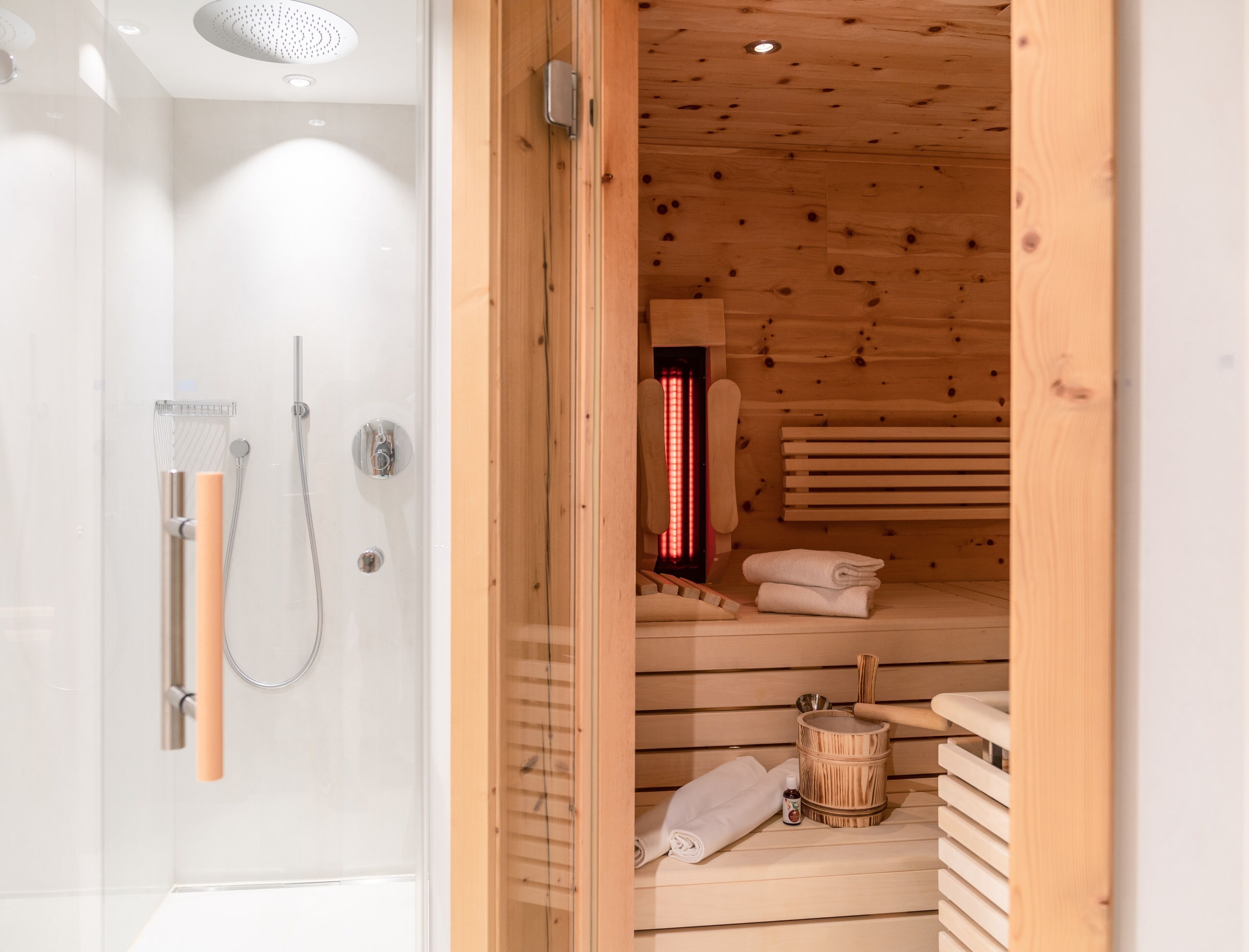 Un baño moderno con cabina de ducha de vidrio, una sauna de madera con banco y un cubo de madera.