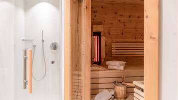Un baño moderno con cabina de ducha de vidrio, una sauna de madera con banco y un cubo de madera.