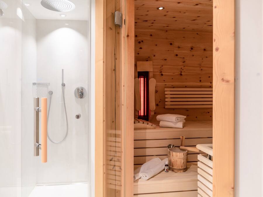 Ein modernes Badezimmer mit Duschkabine aus Glas, ein Saunaraum mit Holzbank und ein Holzeimer.