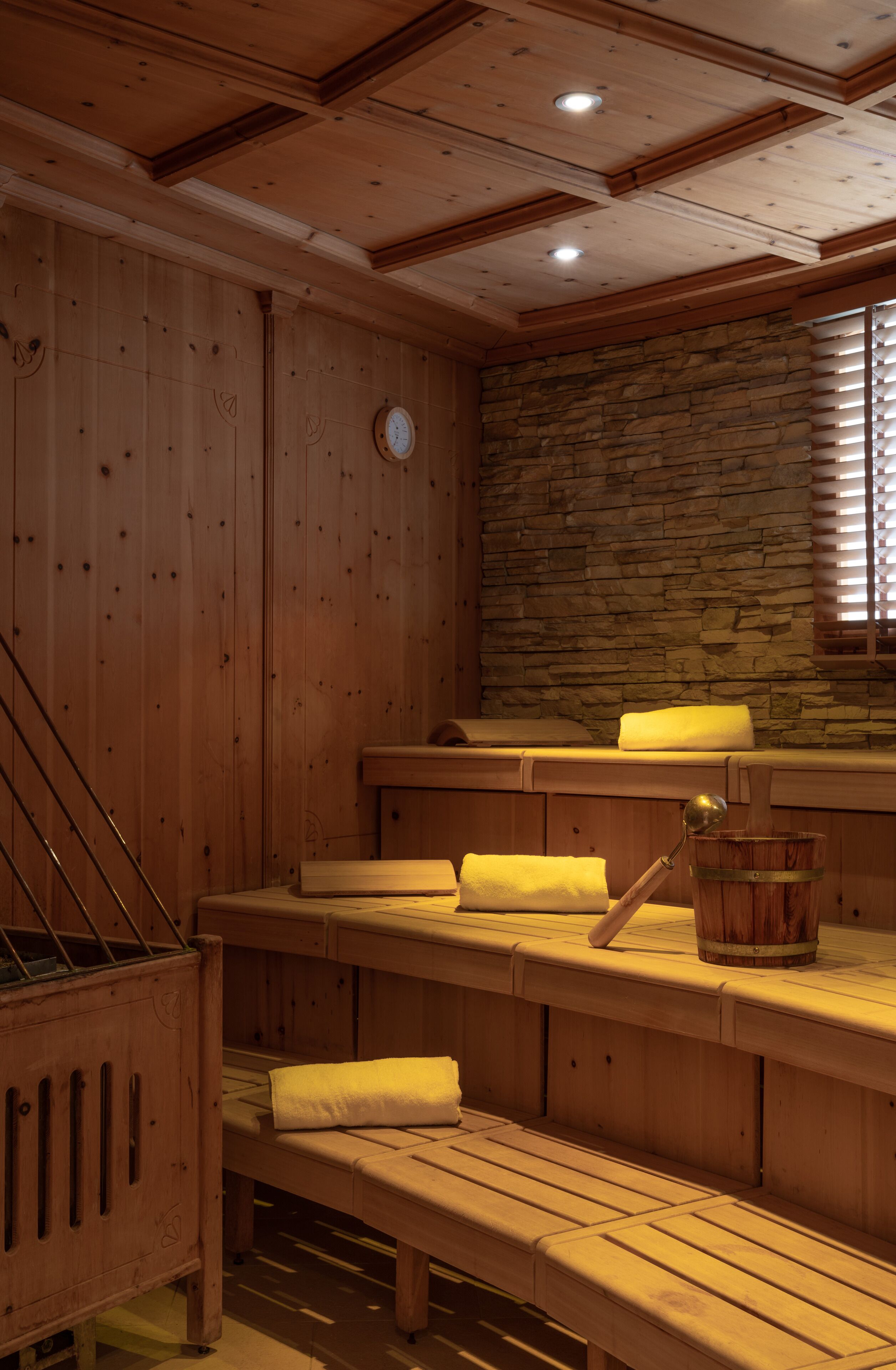 A sauna room with wooden benches, a stone wall, and a wooden cabinet.
