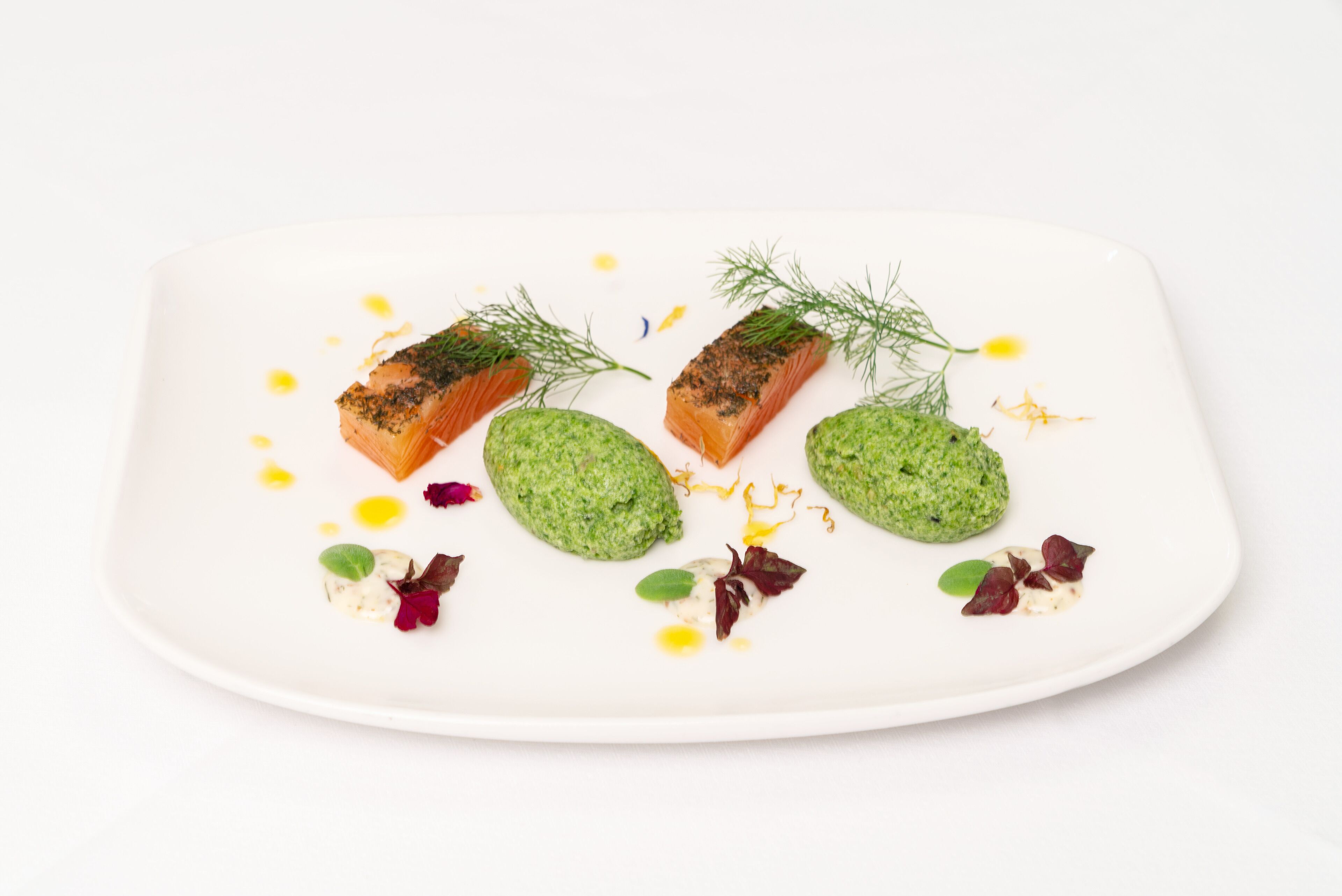 A white plate with salmon and green sauce, garnished with herbs and edible flowers.