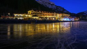 Un grand hôtel à plusieurs étages, avec un télésiège visible au loin, situé au bord d’un lac gelé et offrant une vue sur les montagnes.