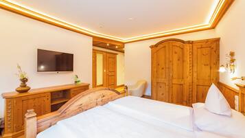 A hotel room with a wooden bed, a flat-screen TV, a wooden wardrobe, and a small desk with a vase.
