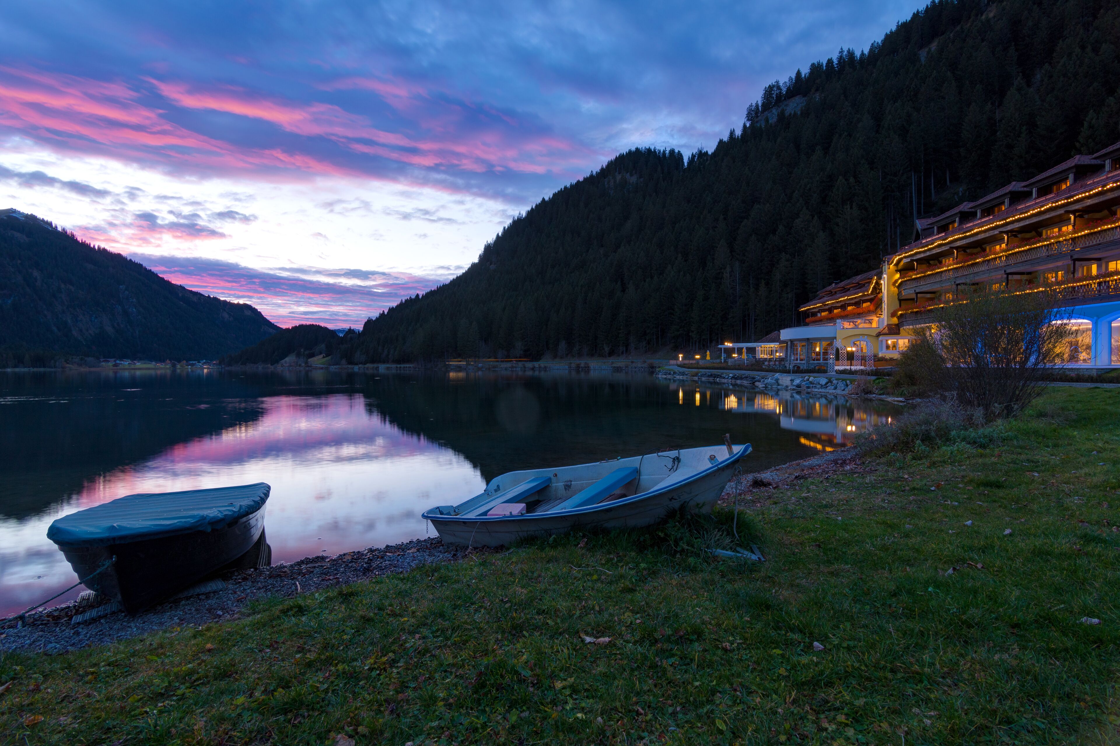 Ein Hotel am Seeufer mit Booten, einem Berg im Hintergrund und Spiegelungen im Wasser.