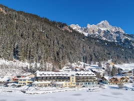 Un complejo turístico en la montaña, cubierto de nieve, con varios edificios, incluyendo un hotel grande con balcones y una zona de piscina.