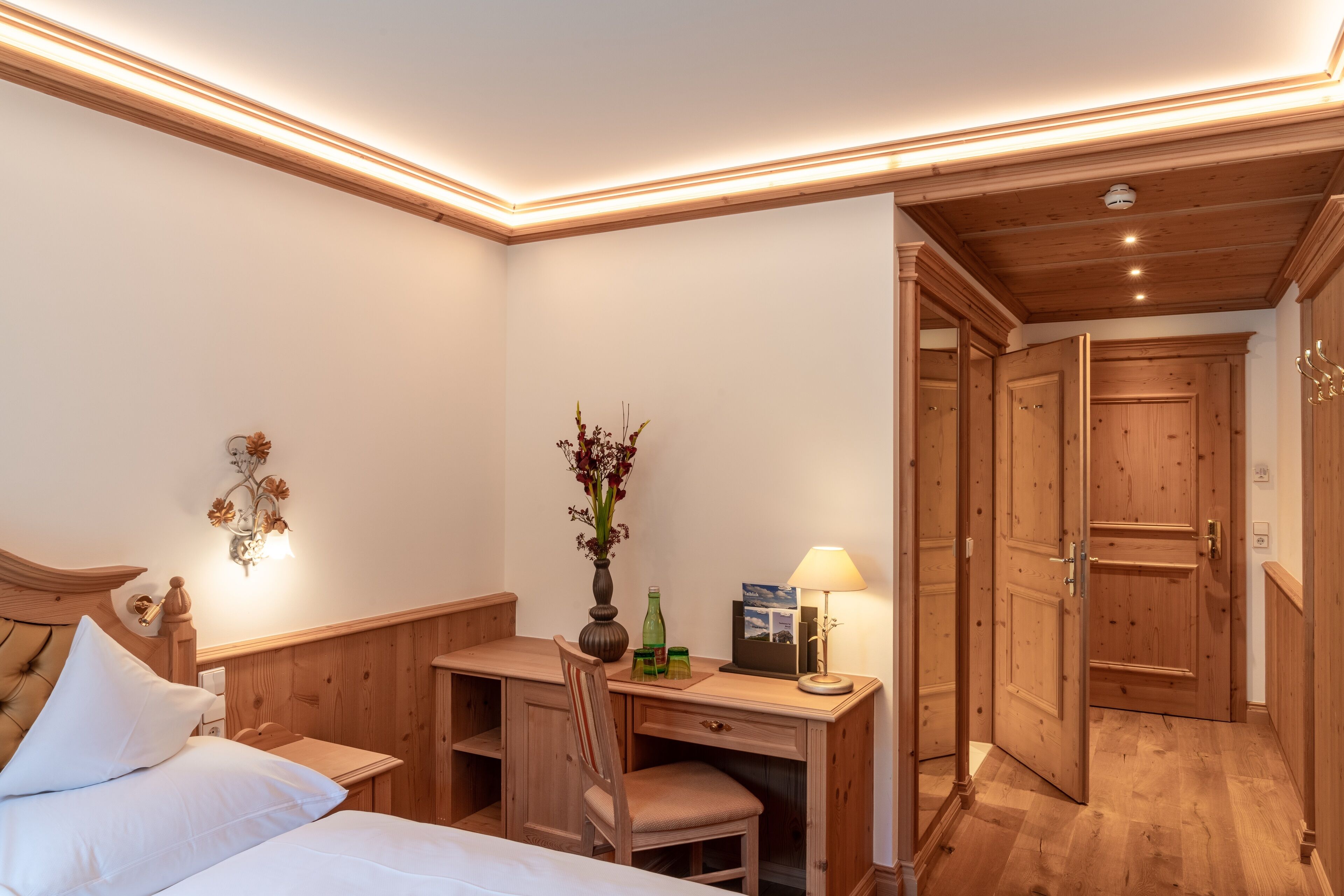 Un dormitorio con cama, escritorio, silla, lámpara y armario de madera.