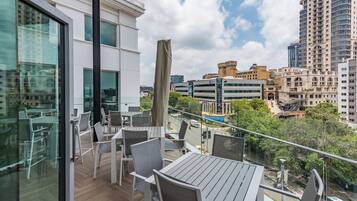 Un balcón con mesa y sillas, con vista a un paisaje urbano de edificios modernos y cielo despejado.