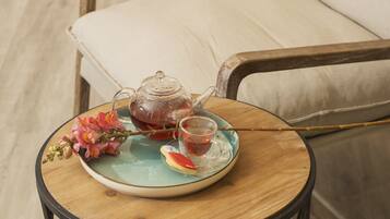 Une table ronde en bois, sur laquelle se trouvent une théière et une tasse en verre, une assiette avec une tranche de fruit et un bouquet de fleurs.