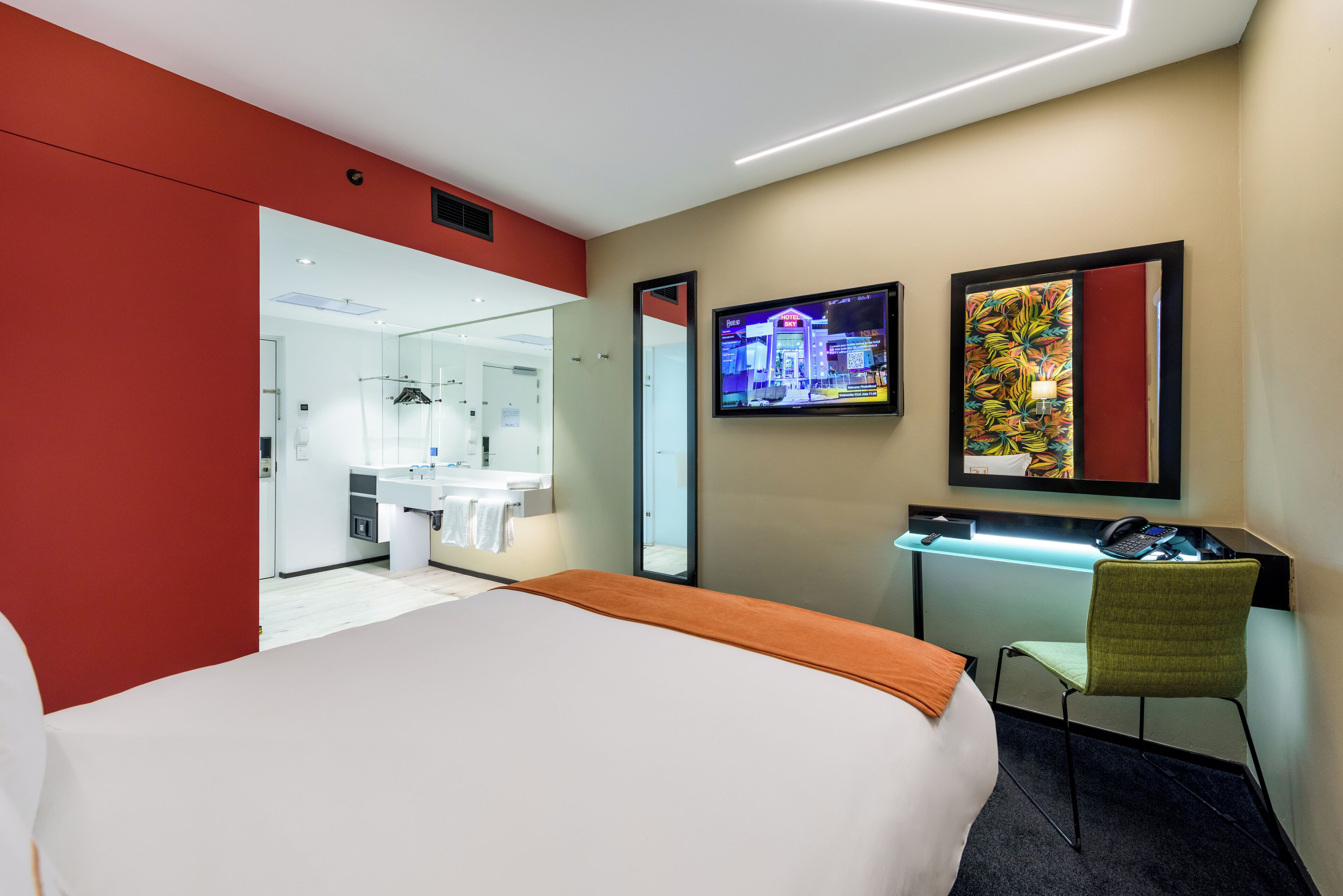A hotel room with a bed, a desk with a chair, a TV, and a bathroom visible through an open door.