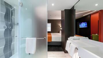 Un baño moderno con cabina de ducha de vidrio, un espejo grande y un lavamanos blanco.