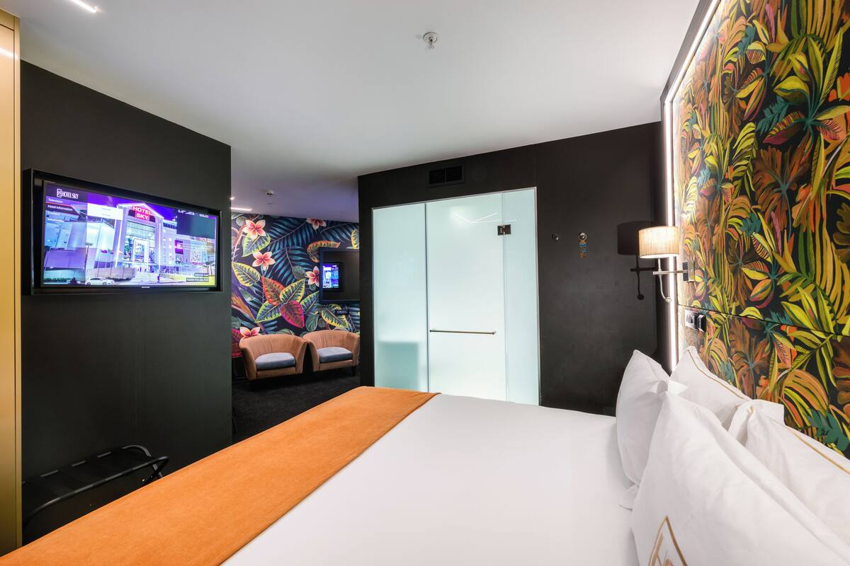 Une chambre d’hôtel avec un lit, un téléviseur fixé au mur, une fresque murale colorée, une porte et une table de chevet.