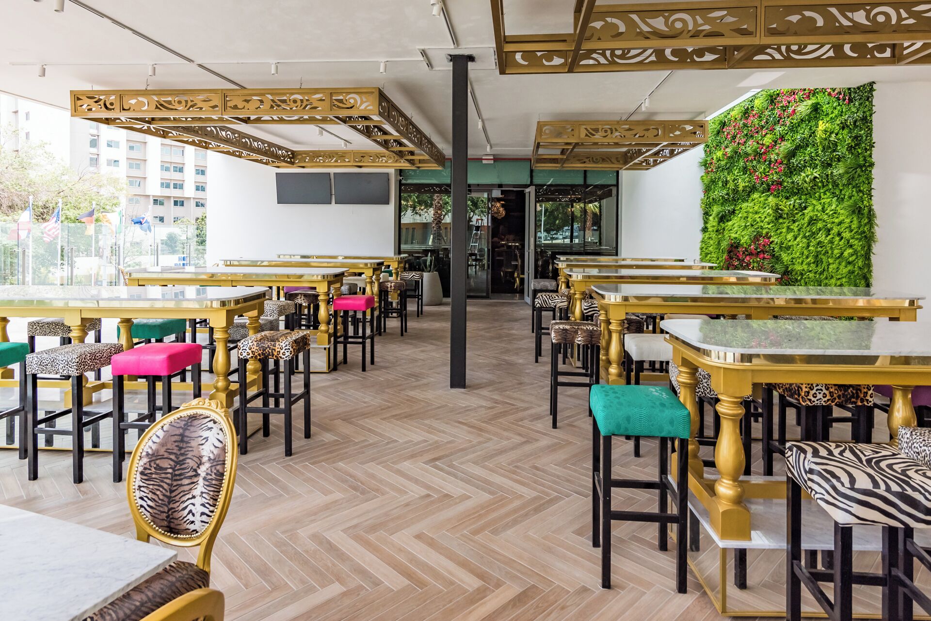 A restaurant with multiple tables and chairs, a herringbone floor, and a green wall with plants.