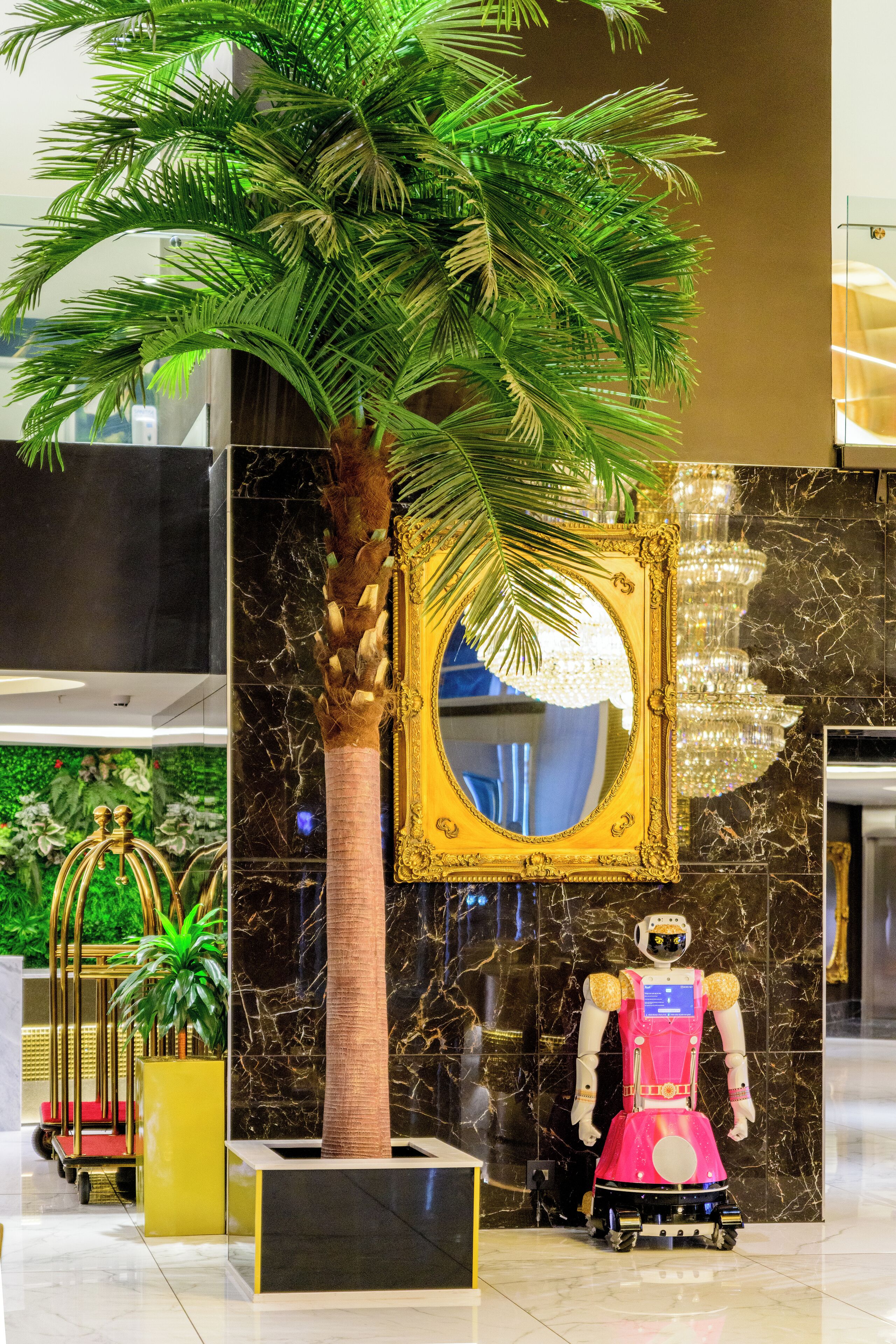 Un vestíbulo con una palmera, un espejo con marco dorado, un candelabro y una figura robótica.