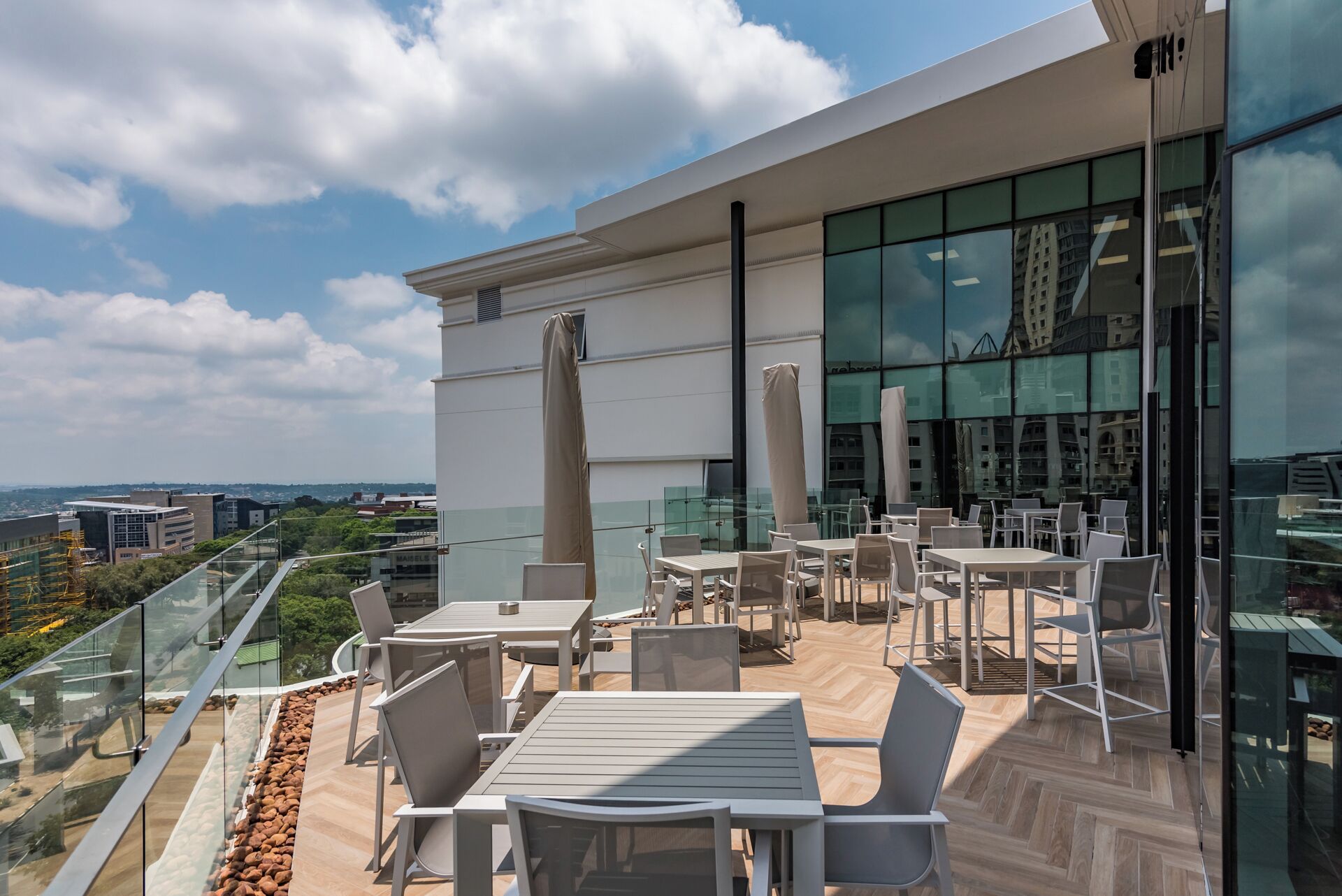 A rooftop terrace with outdoor seating, a glass facade building, and a city view.