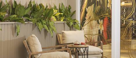 Un interior moderno con dos sillones tapizados, una mesita redonda con tetera y una pared decorativa con plantas y arte abstracto.