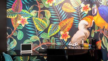 Una habitación con un vibrante mural tropical, un escritorio con una computadora portátil, una cafetera y una silla.