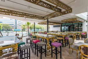 An indoor dining area with high tables and chairs, a view of the street outside, and decorative ceiling panels.