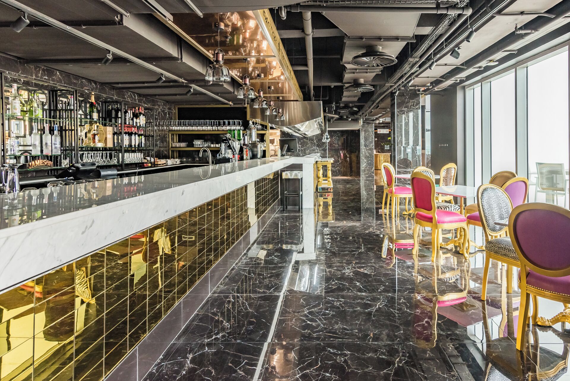 A bar area with a marble countertop, shelves with bottles, and a seating area with chairs.