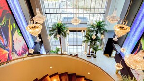 Een moderne hotellobby met een statige trap, grote ramen en decoratieve verlichting.