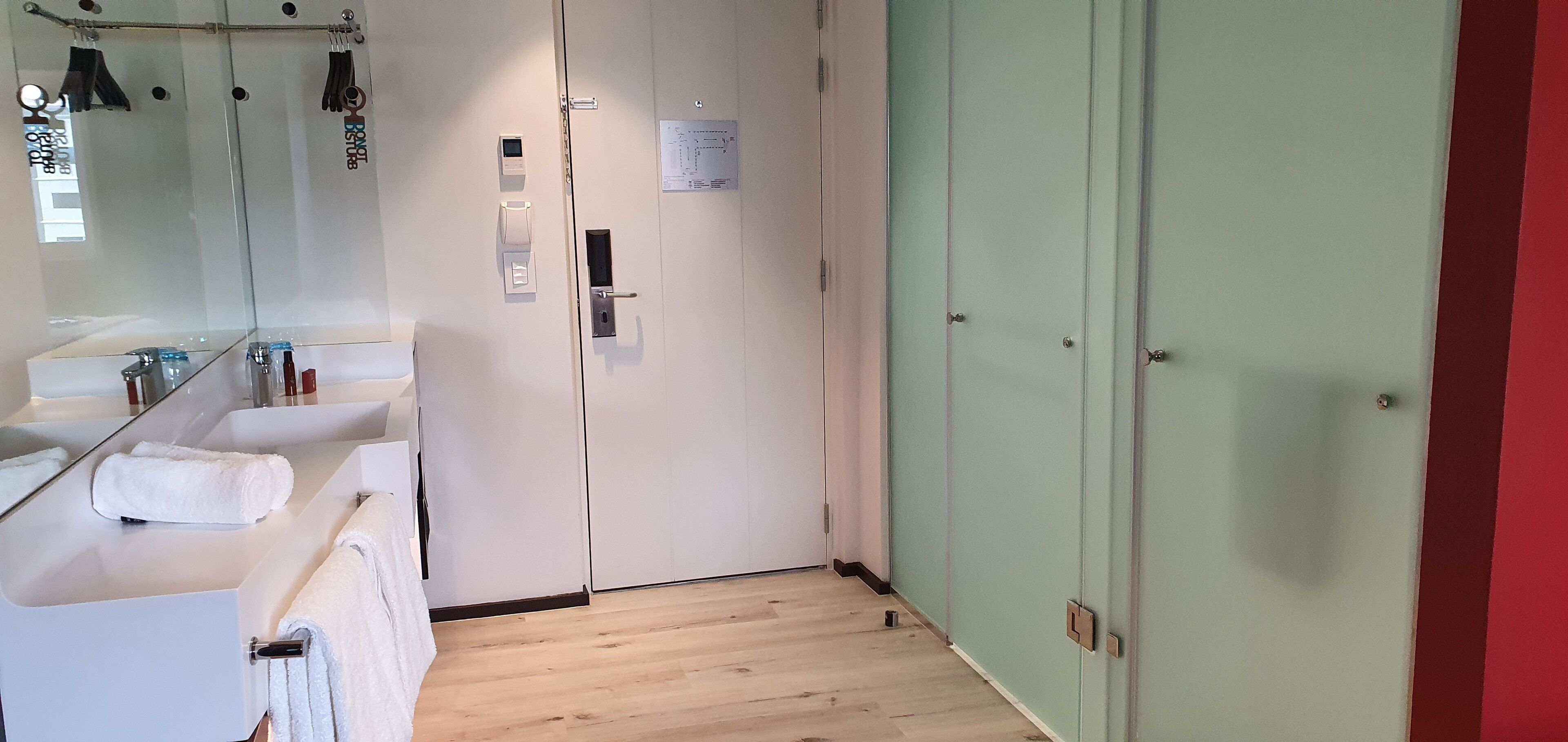 Un bagno moderno con box doccia in vetro, un lavandino bianco con un asciugamano e una porta verde.