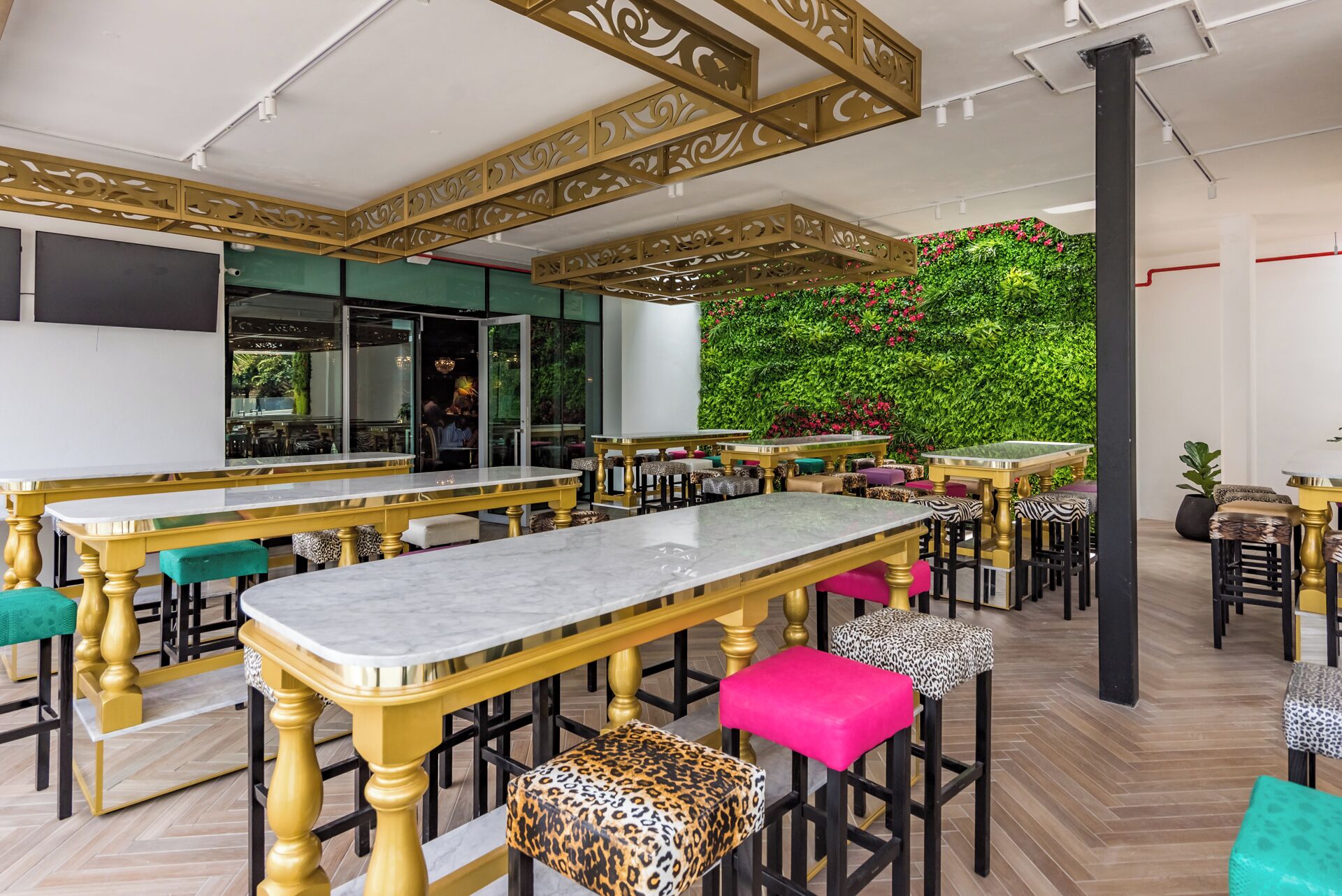 A modern bar area with marble-topped tables and chairs, a green wall with plants, and a decorative ceiling.