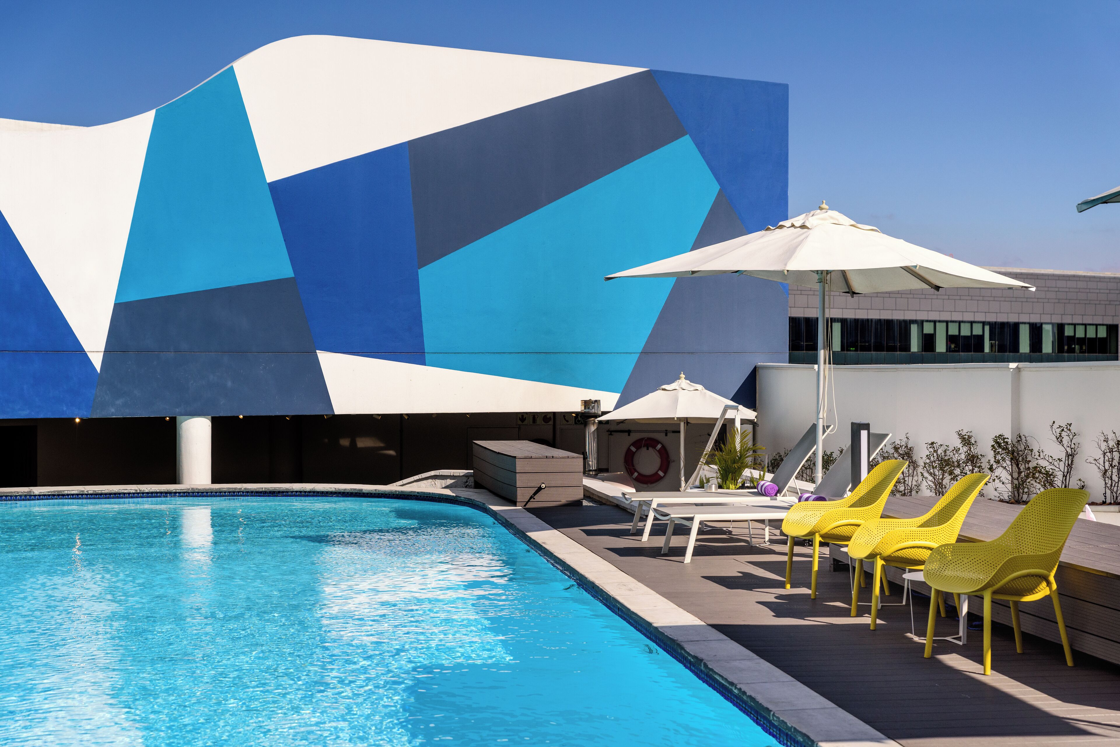 A swimming pool with a geometric facade, yellow lounge chairs, and a lifebuoy.
