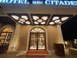 El exterior del Hotel MBC Citadel, con una entrada destacada, ventanas amplias y una fachada bien iluminada.