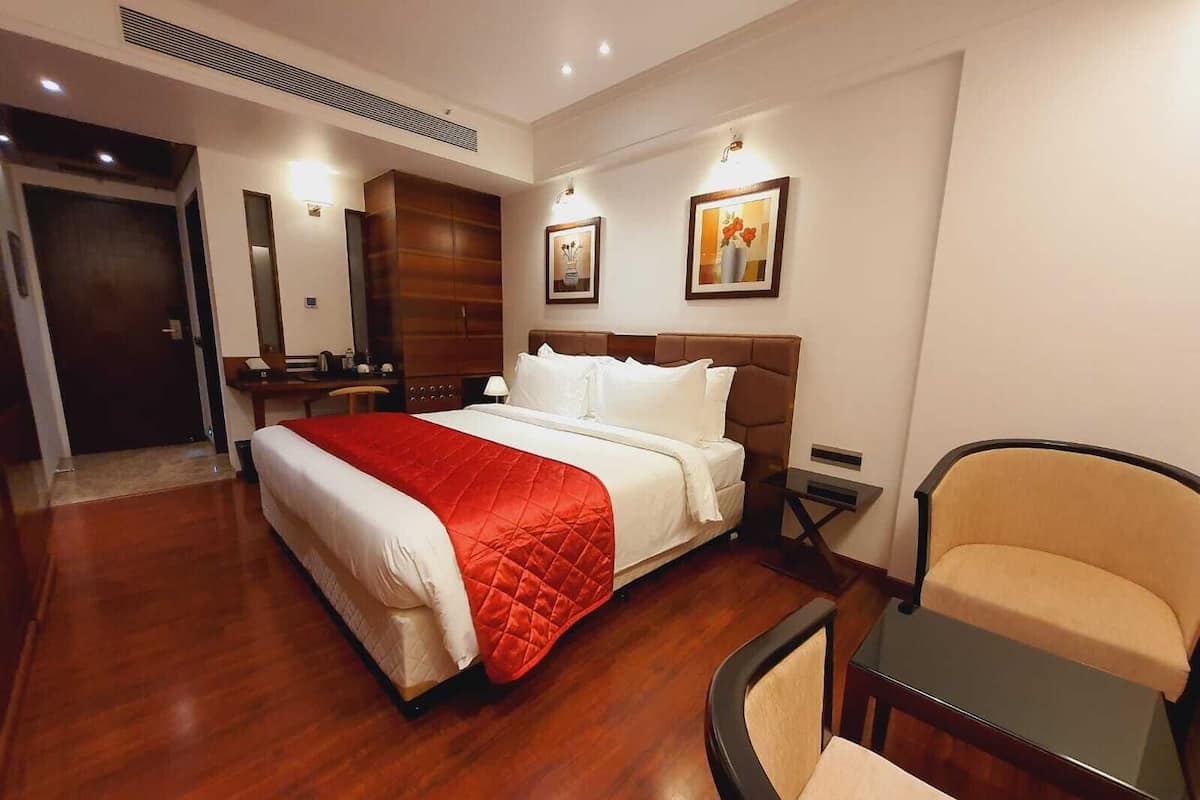A hotel room with a large bed, a desk, a chair, and a wardrobe.