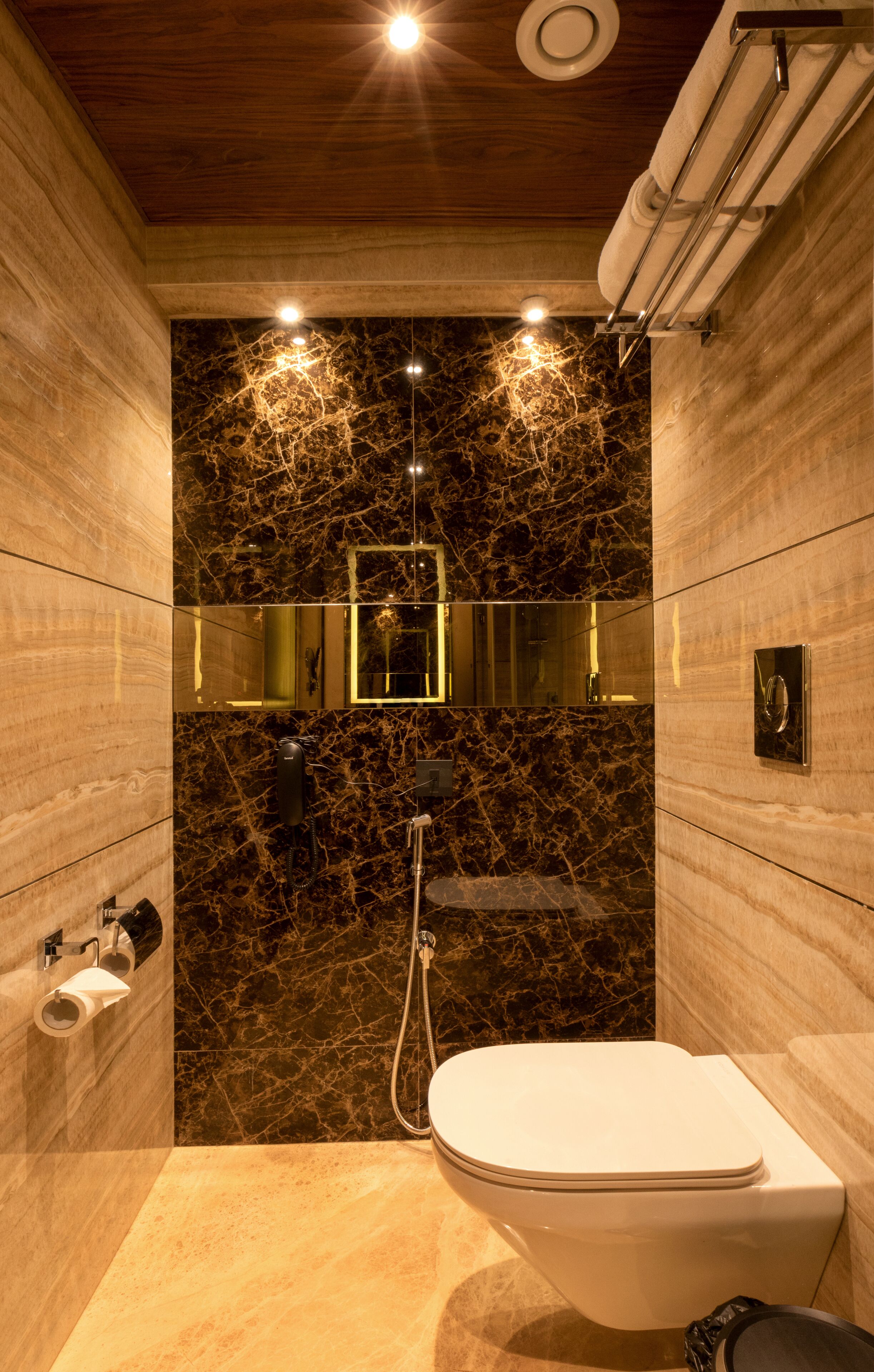A modern bathroom with a marble wall, a toilet, a shower, and a mirror.