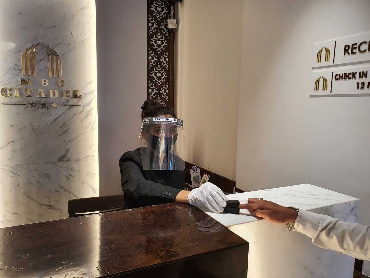 A hotel reception desk with a marble wall and a sign indicating check-in at 12 PM.