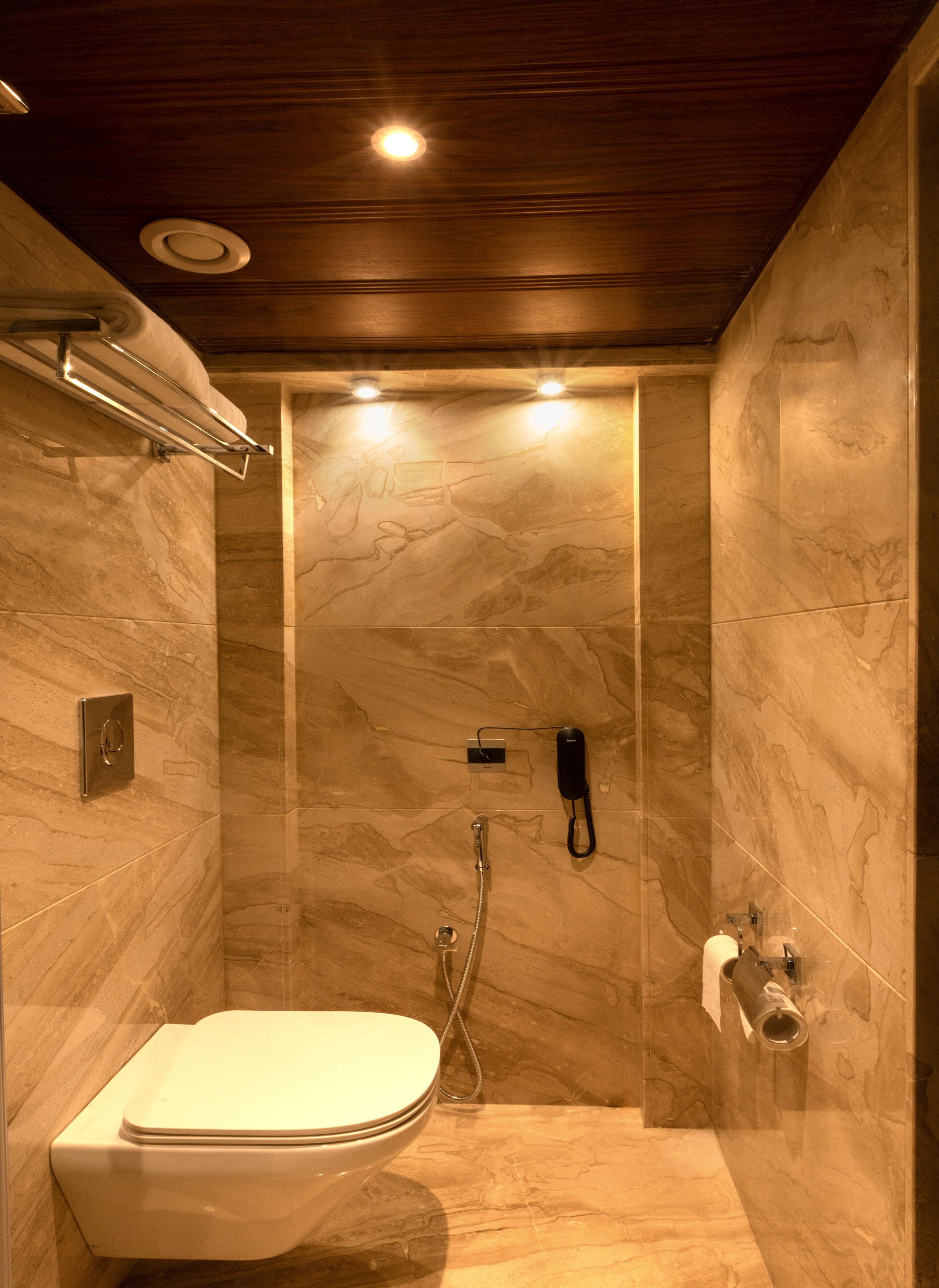 A modern bathroom with a marble wall, a toilet, a shower, and a phone mounted on the wall.