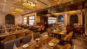 A spacious dining area with multiple tables set for service, elegant chandeliers, and large windows providing natural light. - Hotel MBC Citadel Nashik (Nashik)