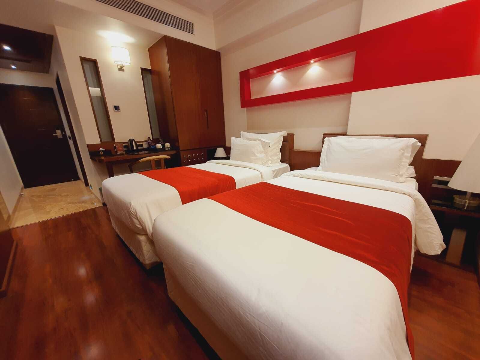 Habitación de hotel con dos camas, un escritorio, un espejo y una pared decorada en rojo.