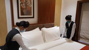A hotel room with a neatly made bed, a framed floral artwork on the wall, and a wooden headboard.
