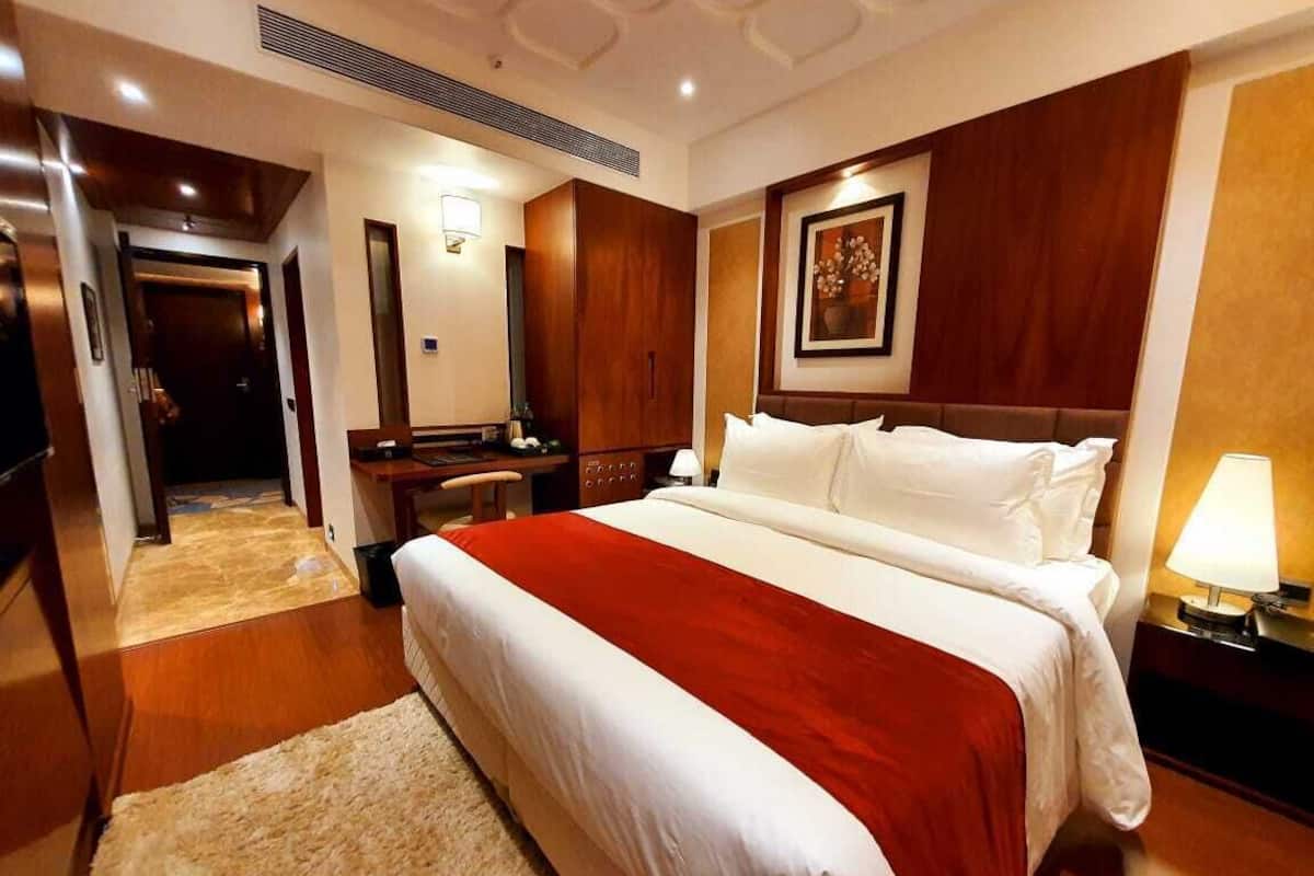 A hotel room with a large bed, a desk, a chair, a lamp, and a framed picture on the wall.