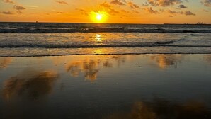 Een strand met de ondergaande zon boven de horizon, weerspiegeld in het natte zand.