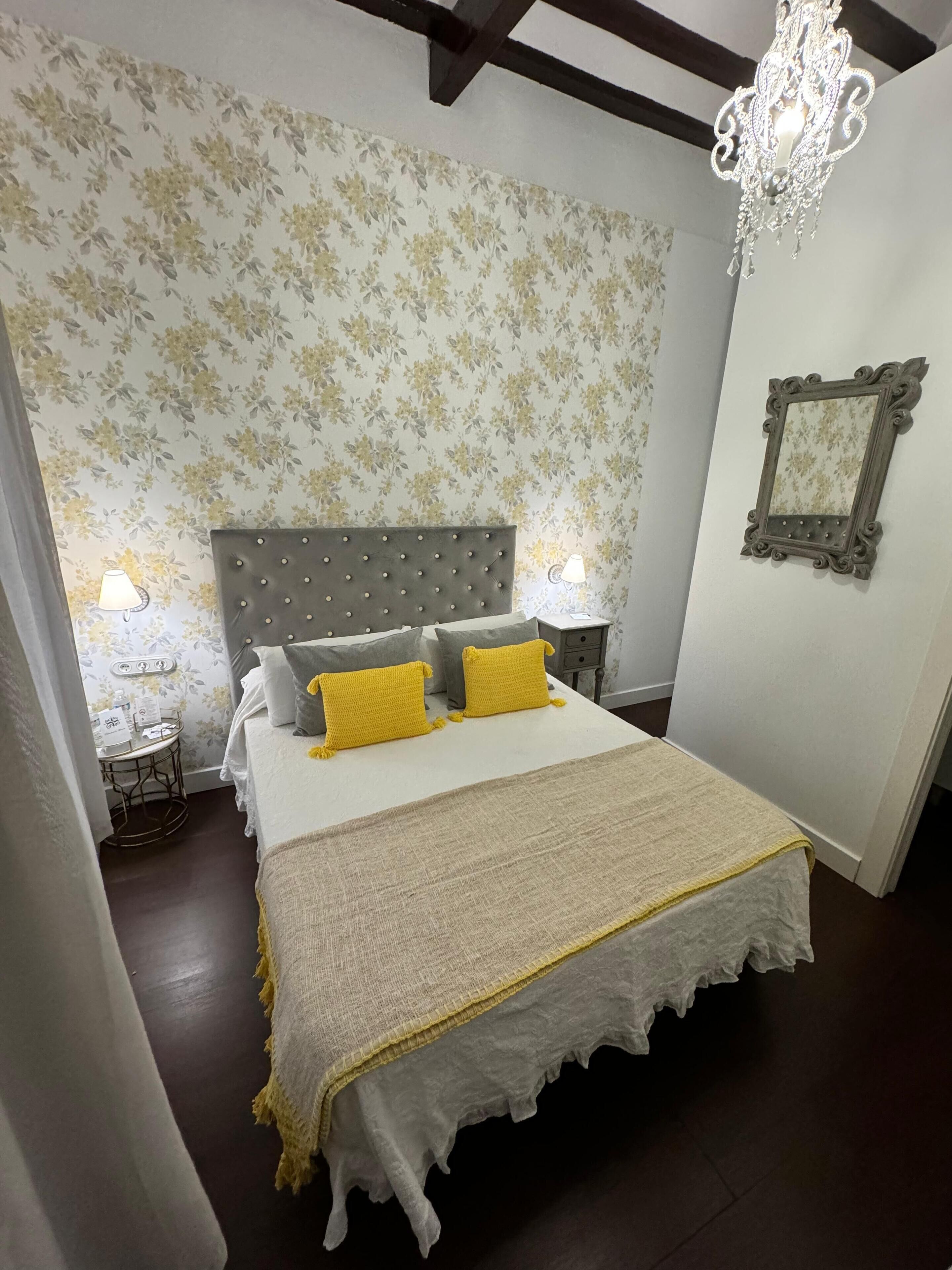 Un dormitorio con una cama grande, papel tapiz floral, un candelabro y un espejo en la pared.