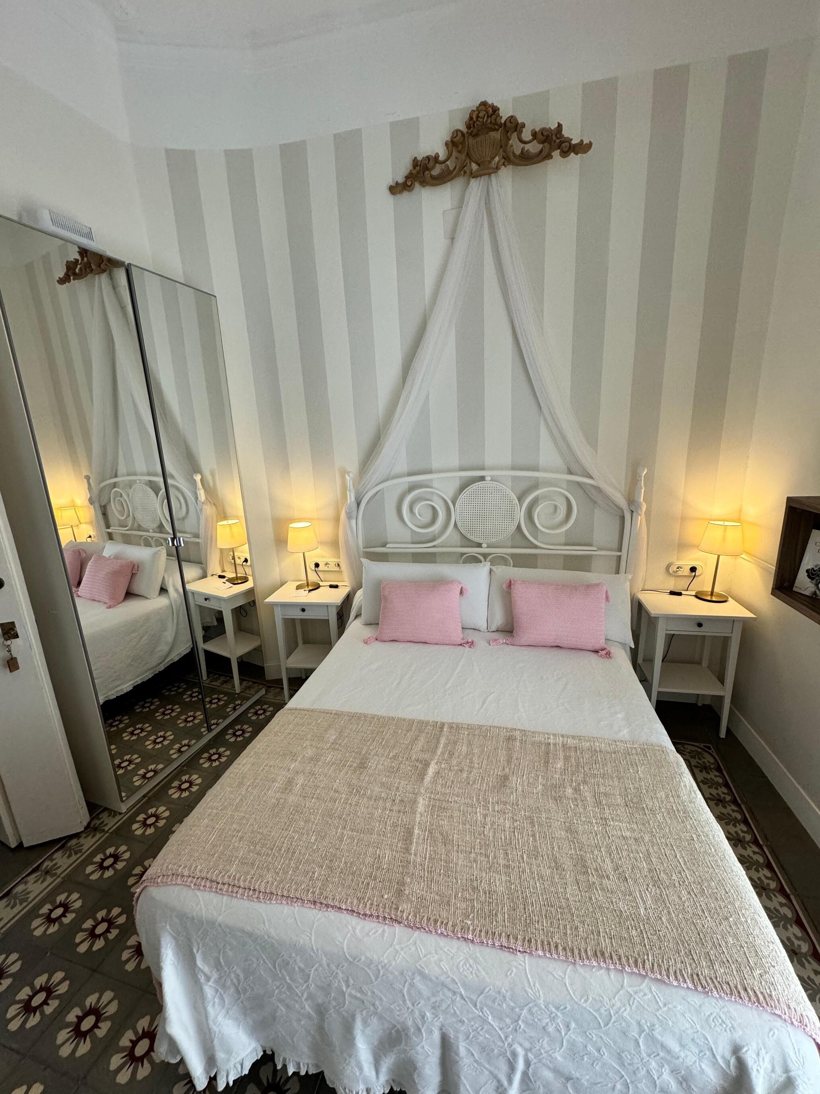 A hotel room with a large bed, two bedside tables with lamps, a mirror, and a striped wall.