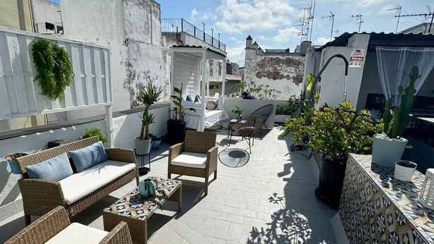 Een terras op het dak met rieten meubilair, potplanten en een decoratieve muur.
