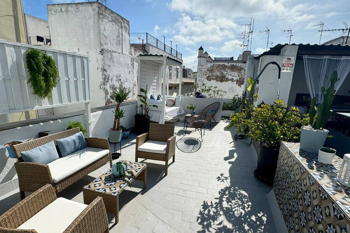 Terraza en la azotea con mobiliario de mimbre, plantas en macetas y un muro estampado.