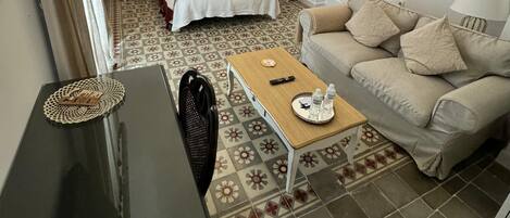 A hotel room with a bed, a sofa, a small table, a chandelier, and a patterned floor.