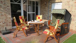 Une terrasse extérieure avec un sol en briques, une table et quatre chaises dotées de coussins colorés.