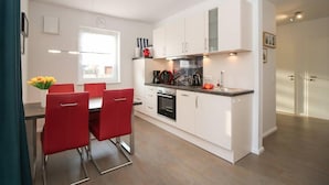 Une cuisine moderne avec des armoires blanches, un four encastré et un coin repas doté de chaises rouges.