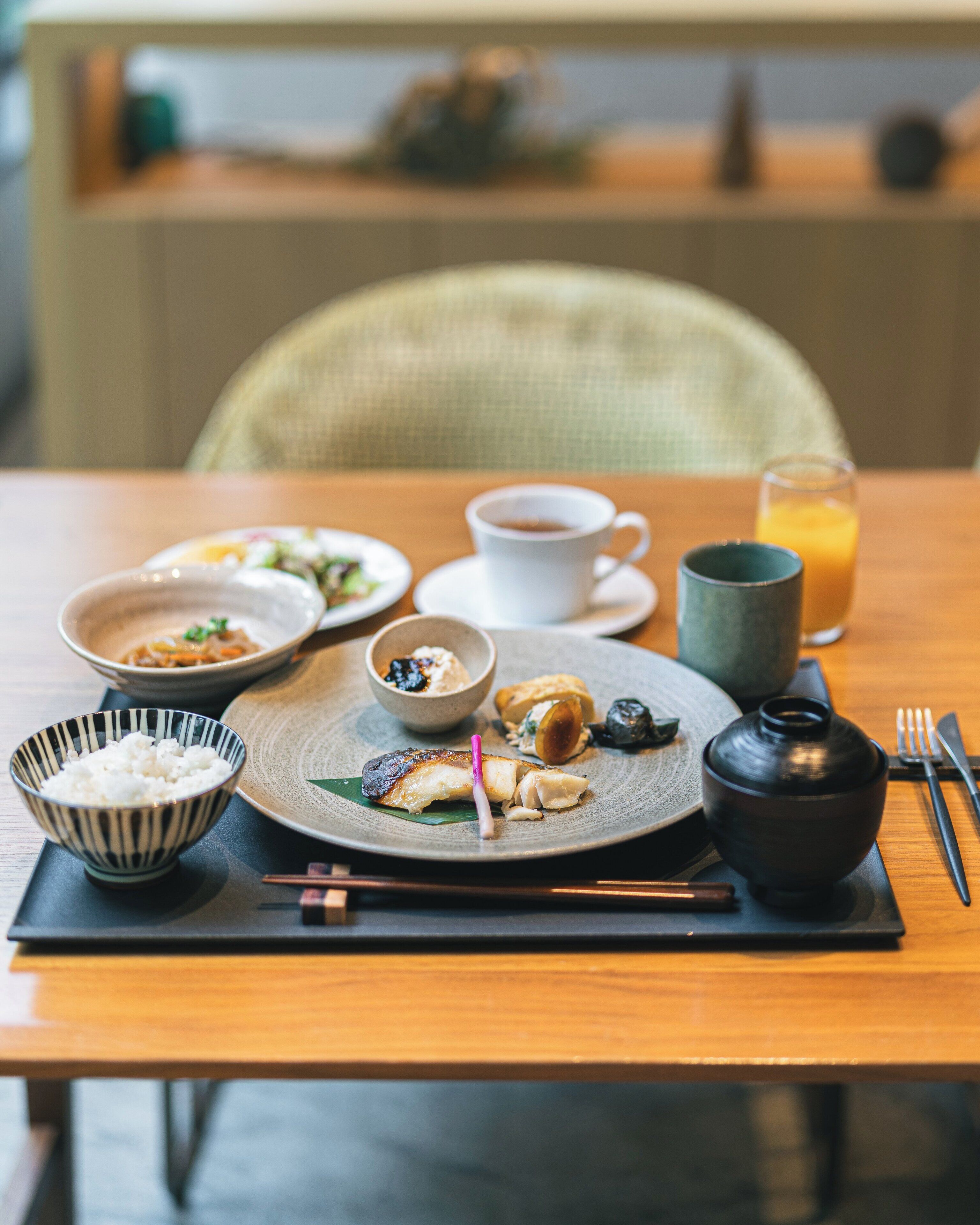 A dining table with various dishes, a cup of coffee, a glass of orange juice, and traditional Japanese utensils.