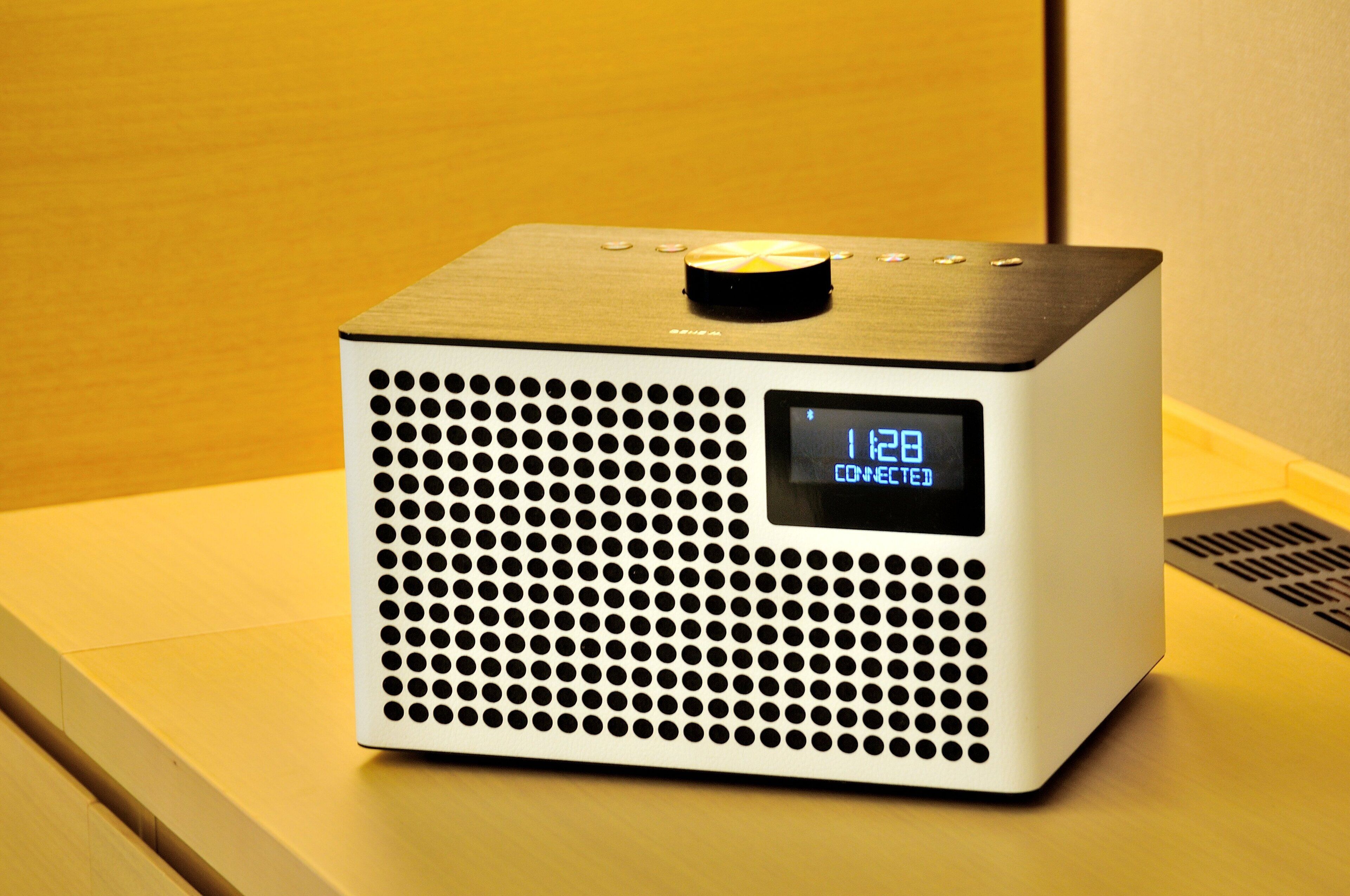 Un altavoz moderno de forma cuadrada con una pantalla digital en la parte frontal, sobre una superficie de madera.