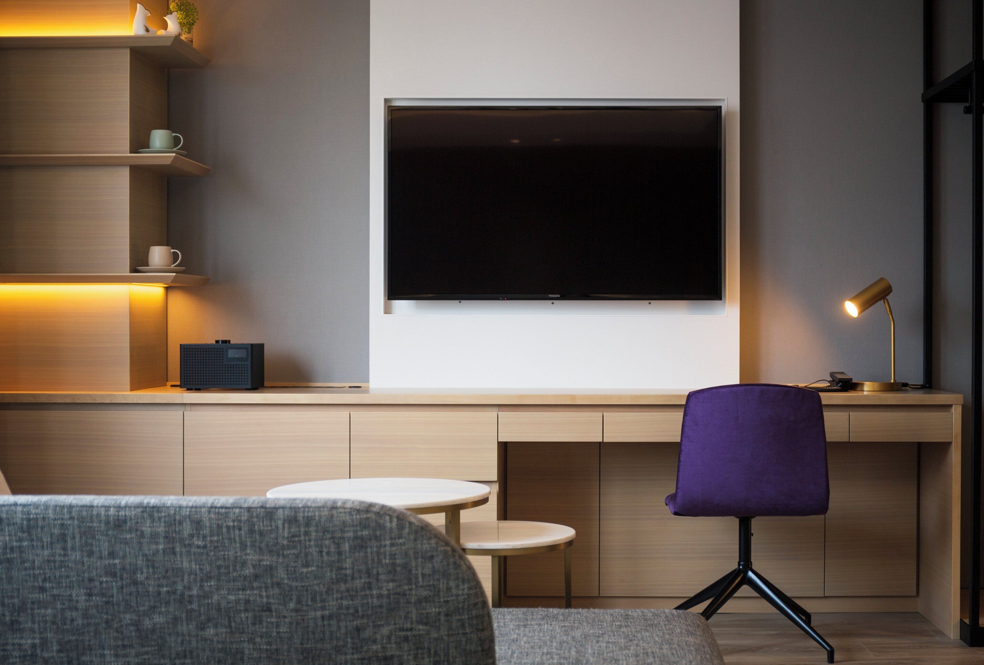 A modern living room with a large flat-screen TV mounted on the wall, a purple chair, a small round table, and a coffee table.