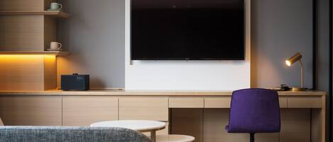A modern living room with a large flat-screen TV mounted on the wall, a purple chair, a small round table, and a coffee table.