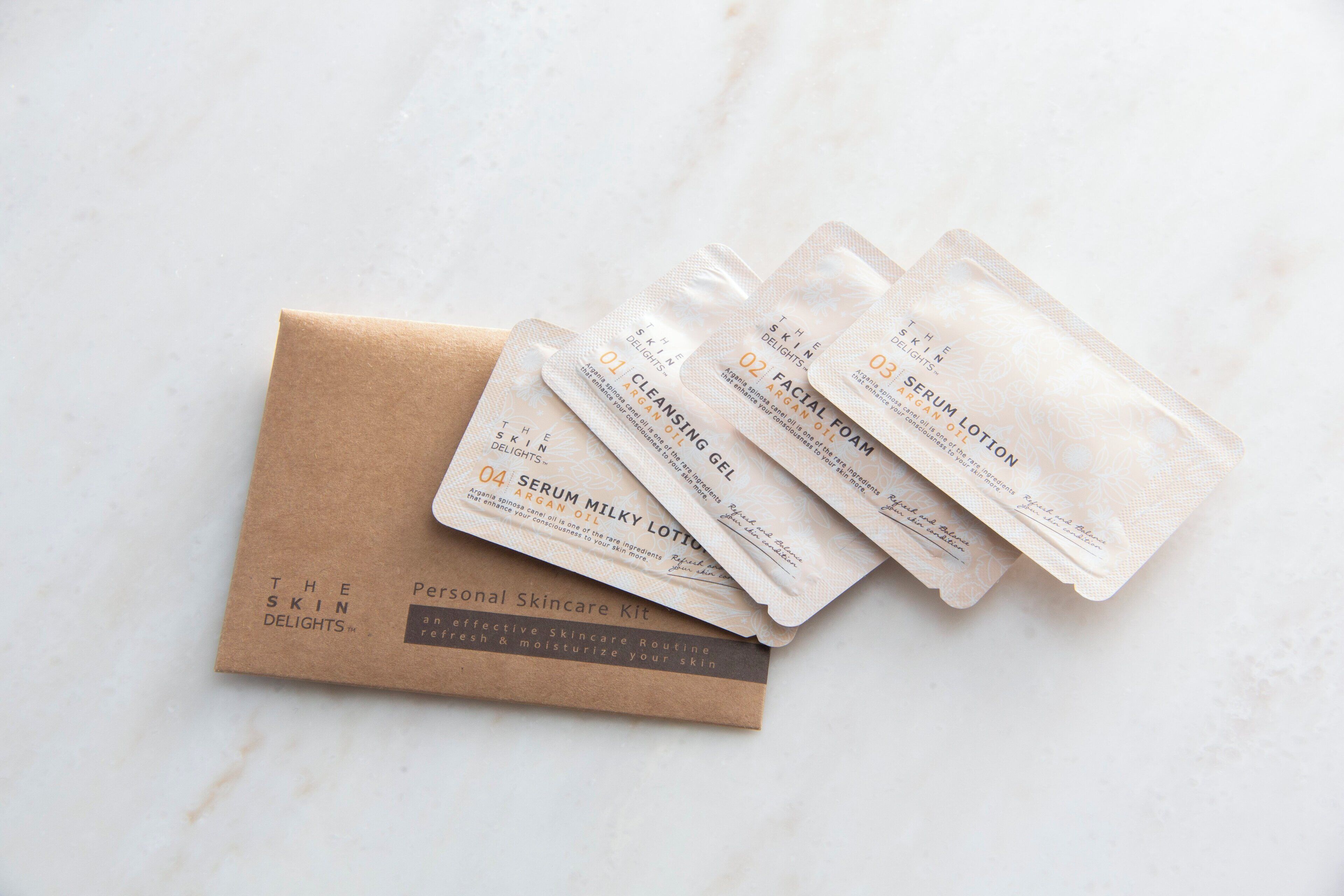 Una bolsa de papel marrón con la etiqueta "The Skin Delights" contiene cuatro paquetes de productos para el cuidado de la piel etiquetados como "Serum Lotion" y "Serum Milky Lotion" sobre una superficie de mármol.