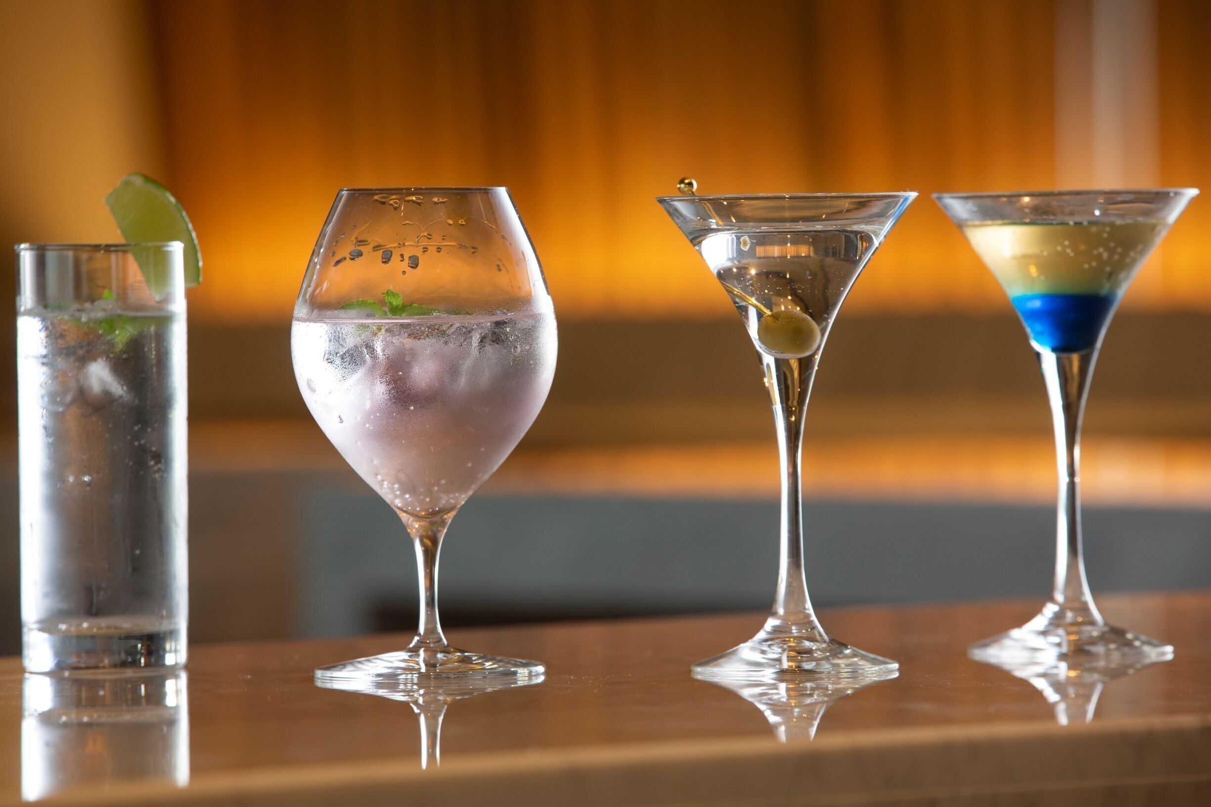 Four different types of glasses with various drinks on a reflective surface.
